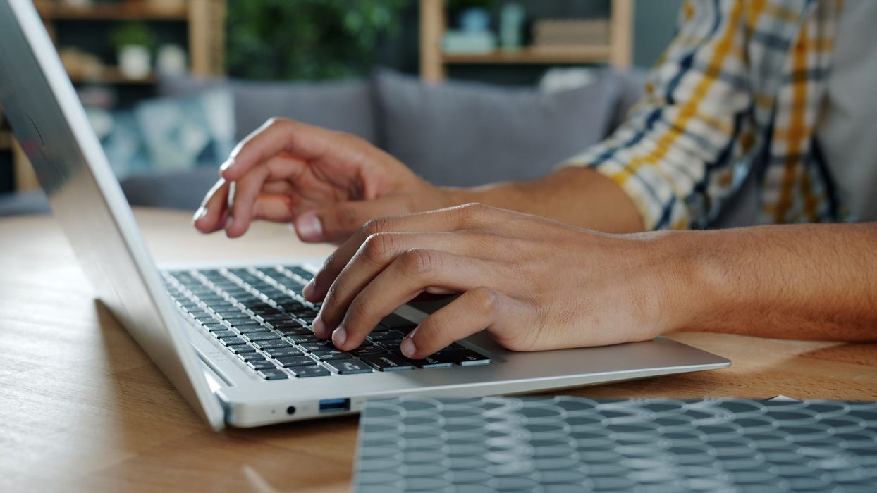 Close-up of hands typing on a laptop keyboard beside a notebook